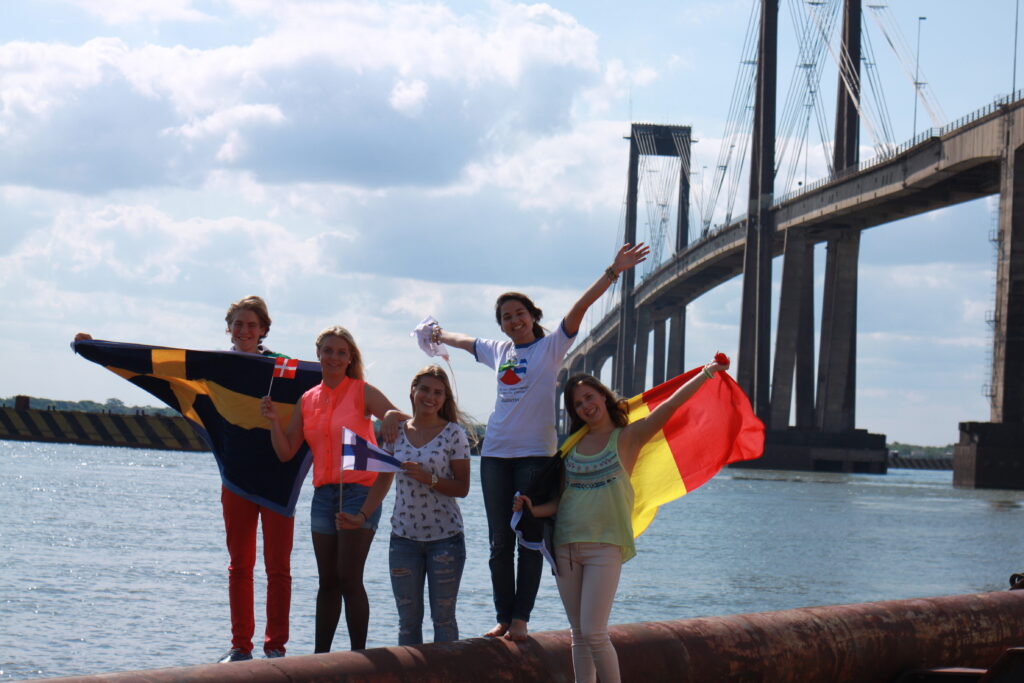 Vaihto-oppilaat eri maista poseeraamassa lippujensa kanssa ison sillan edessä
